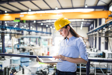 Female project manager standing in modern industrial factory. Manufacturing facility with robotics,...