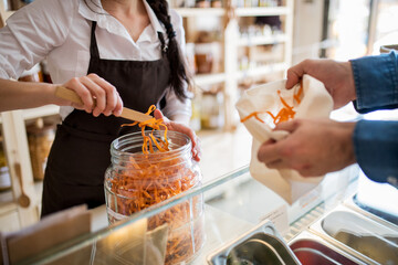 Shop assistant serving customer in package-free store using reusable containers. Zero waste shops...
