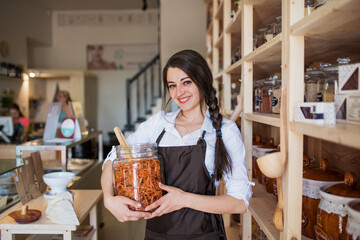 Shop assistant serving customer in package-free store using reusable containers. Zero waste shops...