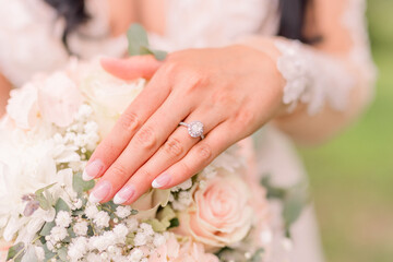 A bride is married and shows her engagement ring over her soft bridal flowers. She wears a lace outfit. 