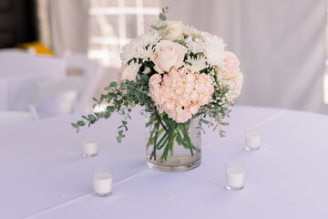 A beautiful bouquet with pink hydrangeas and soft white roses on a white tablecloth table with small candles 