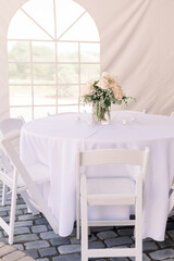 A tented backyard wedding reception with a white table and a simple wedding floral centerpiece.  