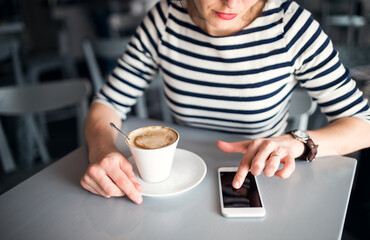 Happy young woman using mobile phone and enjoying coffee at cafe.