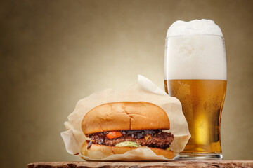 A glass of light, frothy beer with a burger on a wooden board. Selective focus