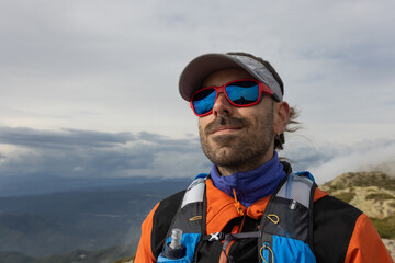 A man wearing sunglasses and a red cap is standing on a mountain