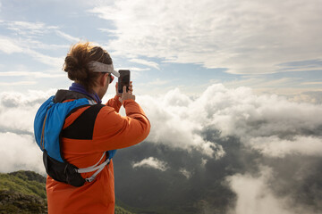 A woman is taking a picture of the mountains with her cell phone
