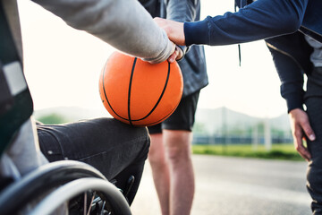 Disabled young man in a wheelchair playing basketball with his friends. Teamwrok and male...