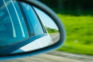 reflection of a country road in the rear view mirror of a car. traveling by car