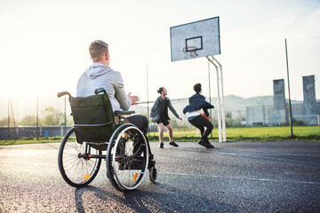 Disabled young man feeling excluded, want to play basketball with his friends, but because of wheelchair he can't.