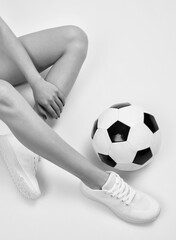 Beautiful sexy girl in a white tracksuit with a black and white soccer ball against a white background.