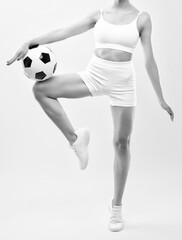 Beautiful sexy girl in a white tracksuit with a black and white soccer ball against a white background.