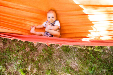 The baby is lying in a rocking hammock during a warm summer day.