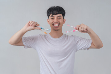 Handsome young man holding several colorful toothbrushes.