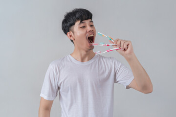 Handsome young man holding several colorful toothbrushes.