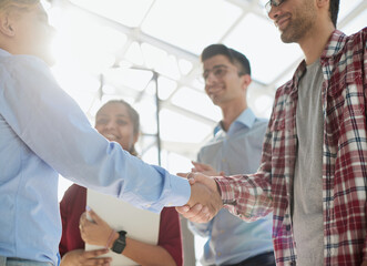 Obraz premium Young startup in casual clothes shaking hands in a modern office space by the window.
