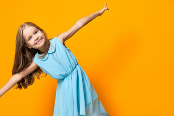 Joyful little girl in a blue dress jumping energetically against a vibrant orange background