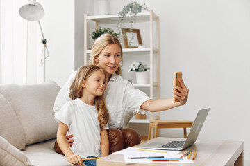Mother and daughter smiling on a cozy couch taking a fun selfie with a laptop in a warm living room