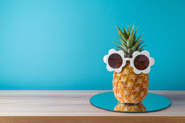 Summer holidays vacation and beach party concept. Pineapple with sunglasses and mirrored tray on wooden table over blue background.