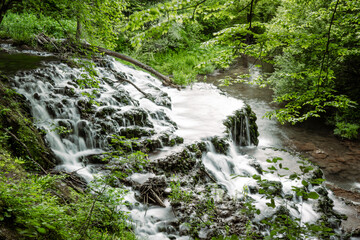 Long Exposure. Surrounded by bright green spring foliage and ferns, waterfall in Bulgaria. cascades over the rocks. Side view.