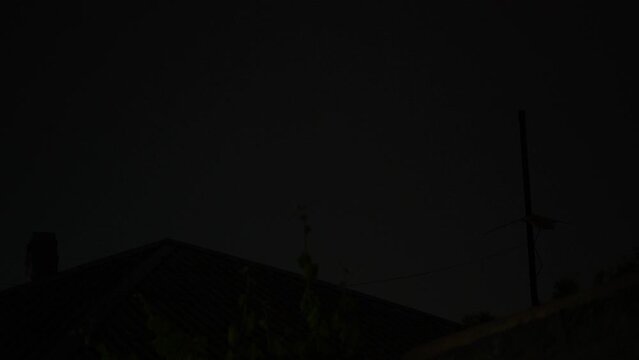 Flashes of lightning over the night street illuminate the house