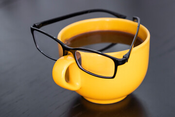 Front view on yellow cup with eyeglasses on it. Creative idea and coffee for business concept	