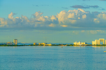 Fototapeta premium Coastal cityscape with modern buildings under a bright sky with fluffy clouds, reflecting on the calm sea. High quality photo. Nichupte Lagoon is one of the best examples of natural paradise. Sunrise