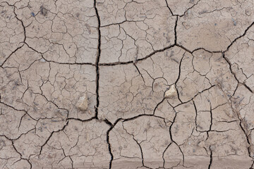 Close-up top view of dry brown cracked clay land surface in a summer day. Abstract weather background. Soft focus. Copy space. Drought and climate change theme.