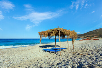 Summer morning pebbly beach with sunbeds and canopy (Borsh, Albania).