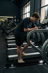 Vertical shot of tired runner male resting after jogging on treadmill during cardio session in gym....