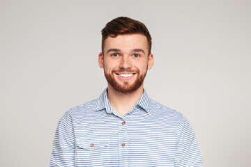Portrait of smiling bearded millennial guy wearing casual shirt posing isolated on beige studio...