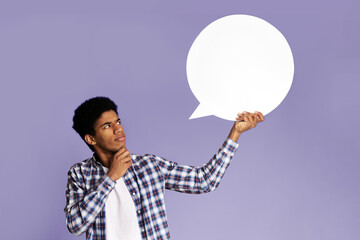 Pensive afro guy looking at blank speech bubble, touching his chin, copy space, pink background
