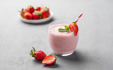 A glass of fresh strawberry smoothie with mint on a blue background with fresh berries.