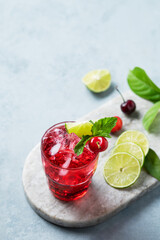 Cherry-lime mojito cocktail with mint, lime and ice on a marble board on a light  background.