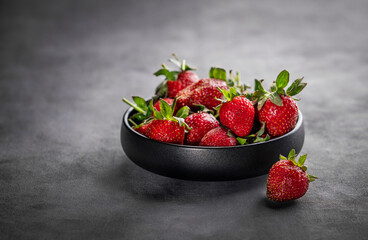 Strawberries in a black bowl on a gray background. The concept of summer natural and healthy farm berries. Сopy space.