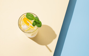 Cold lemonade in a glass with lemon, mint and ice on a yellow blue background  with shadow.