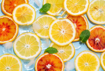 Slices of lemons and blood oranges with ice cubes and mint leaves in water on a blue background.