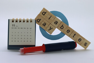 Insulin pen with blue circle and a calendar with the letters in wooden writing Diabetes day 