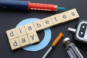 Insulin pen, Glucometer, syringe and insulin vial with blue circle and the phrase diabetes day in wooden with black background 