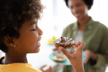 Side view selective focus photo of cute elementary age African American girl eating chocolate...