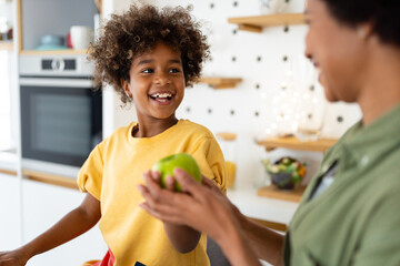Happy smiling young African American girl enjoying healthy habits, having an apple as a snack....