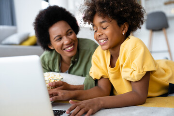 Caring single mother looking proudly at her young smiling female child while using laptop computer...