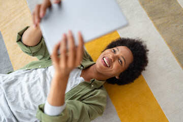 Smiling African American woman using digital tablet while lying on the floor at home.