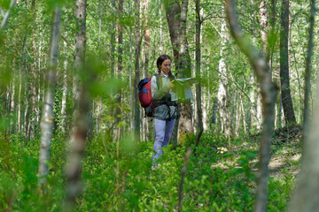 Obraz premium Portrait and wide shoot of young woman looking on the map while crossing hiking trail in spring forest