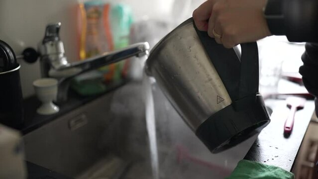 Person cleaning a pot with hot water from the kitchen sink. The image captures a routine domestic chore, emphasizing the practicality and routine of daily life in a home environment