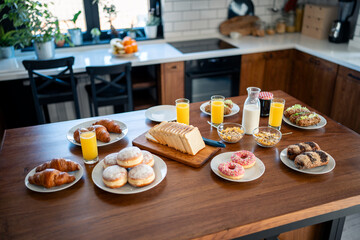Breakfast food table. Festive brunch set, meal variety with donuts, croissants, sandwiches, milk and orange juice. No people on the photo.