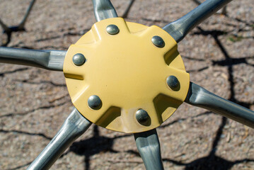 Close-up of the faded yellow metal six-slotted connector of a jungle gym in a park playground