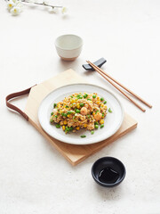 Plate with tasty rice, shrimp and peas, oriental style on minimalist table set, chopsticks and bowl of soy sauce.
