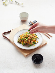 Hand with a handful of green garnish sprinkling on rice dish with prawns and peas on table decorated in oriental style.