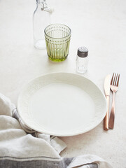 Plate with cutlery served on the table. From above, empty white plate with copper-colored fork and knife placed on the table with salt shaker, glass and water bottle.