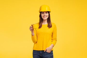 Beautiful smiling middle aged woman engineer wearing yellow hard hat holding yellow cup with drink